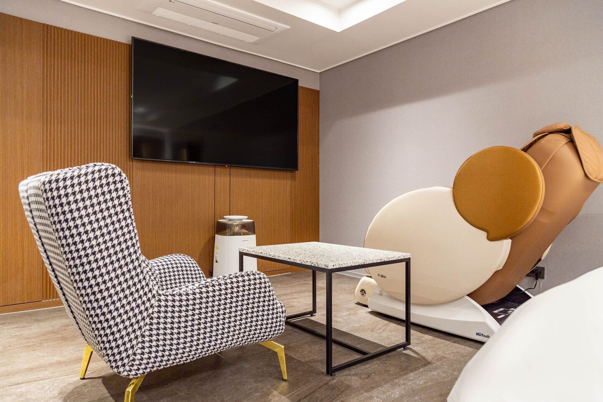 A modern room with a houndstooth patterned armchair, a small table, a large bean bag chair, and a mounted television.