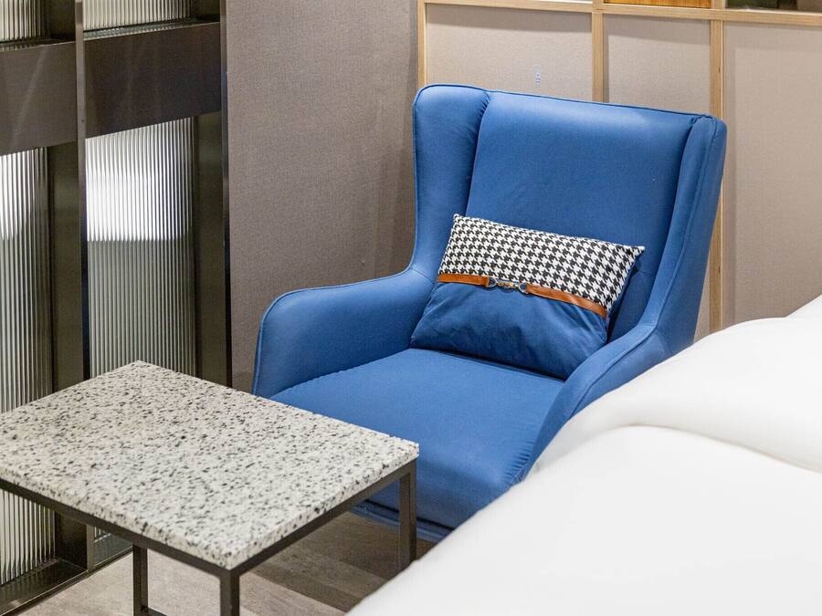 Een blauwe fauteuil met een gekleurd kussen, een klein tafeltje en een witte bank in een moderne kamer met een neutrale kleurenpalet.