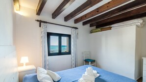 Une chambre à coucher avec un lit, une table de chevet, une fenêtre avec des rideaux, une chaise et une commode blanche.