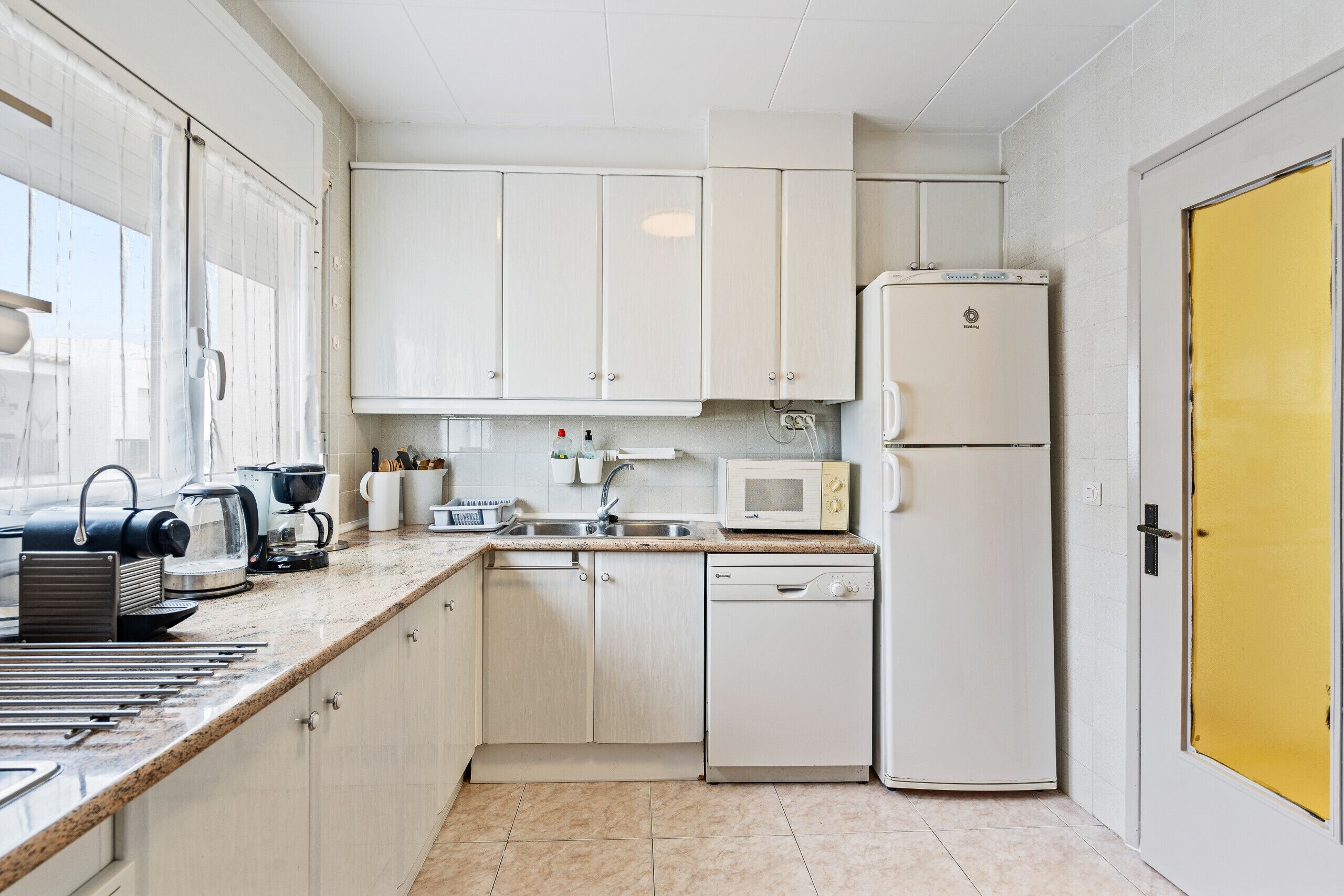 A compact kitchen with white cabinets, a microwave, a dishwasher, and a coffee maker.