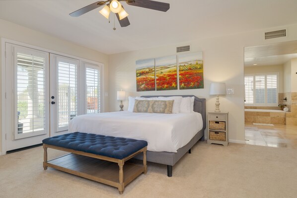 A bedroom with a bed, bench, artwork, nightstand, and a bathroom visible through an open door.