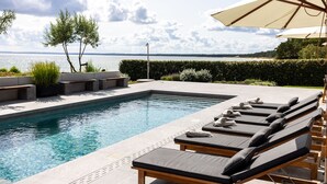 A pool area with lounge chairs and umbrellas, a clear view of the water, and a landscaped garden. - Oakvale Villa Sand (Aahus)