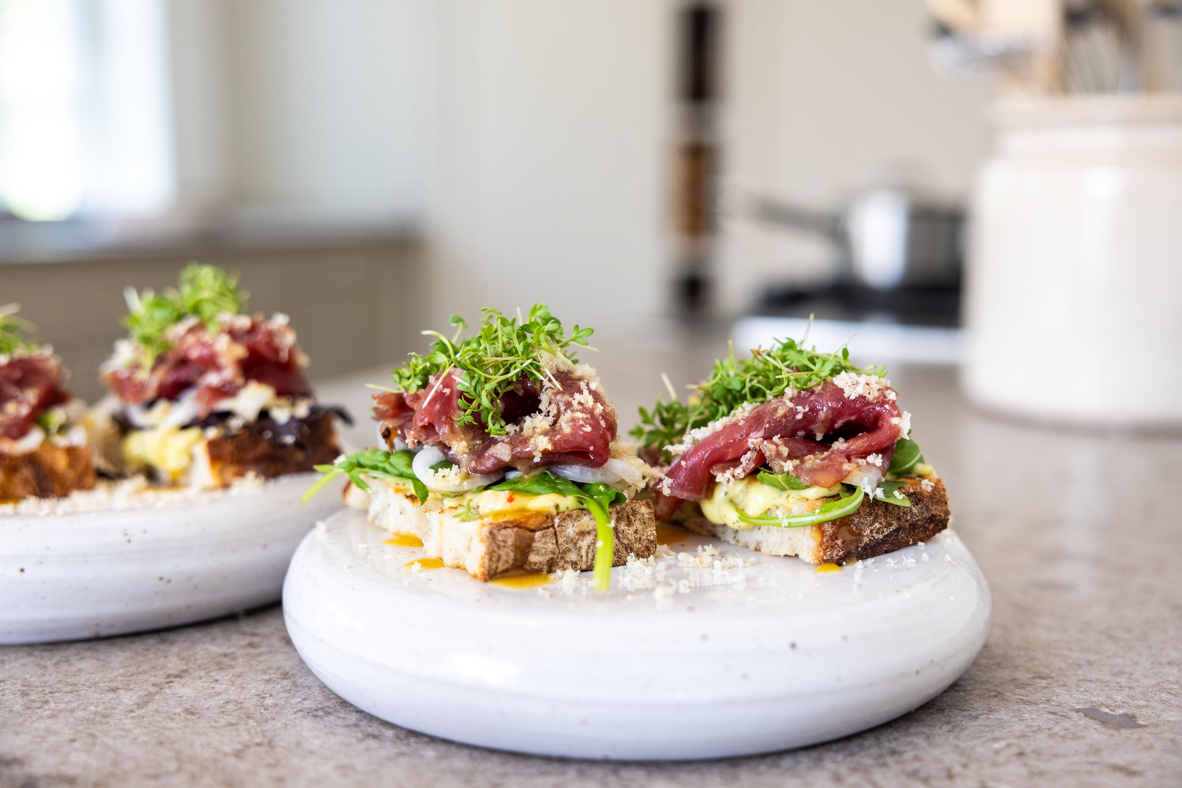 Three appetizers on white plates with a blurred background.