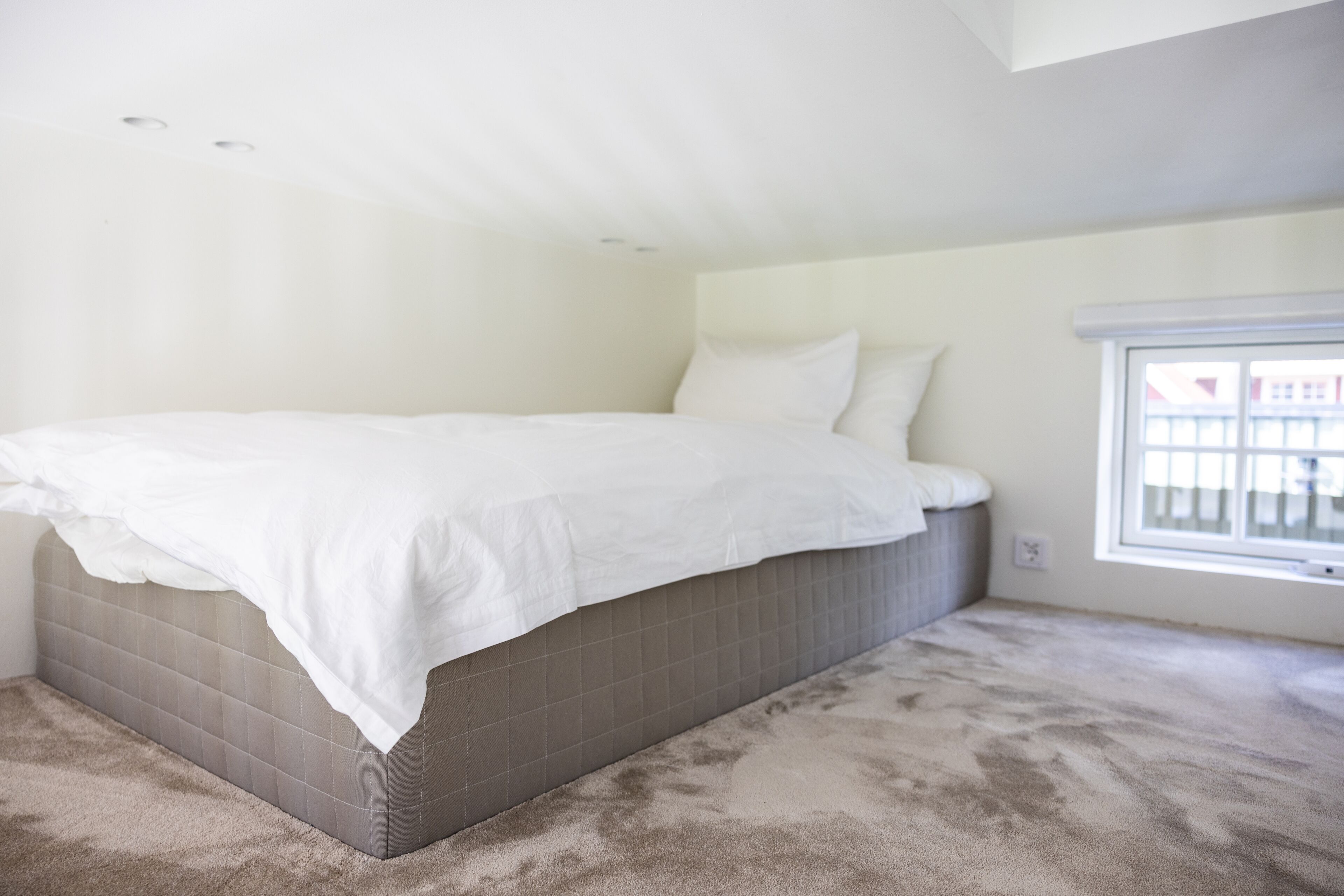 Un dormitorio con una cama grande, una ventana y piso alfombrado.