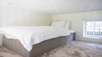 Un dormitorio con una cama grande, una ventana y piso alfombrado.