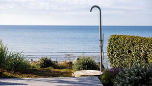 A metal outdoor shower with a curved spout, a wooden deck, and a view of the sea. - Oakvale Villa Sand (Aahus)