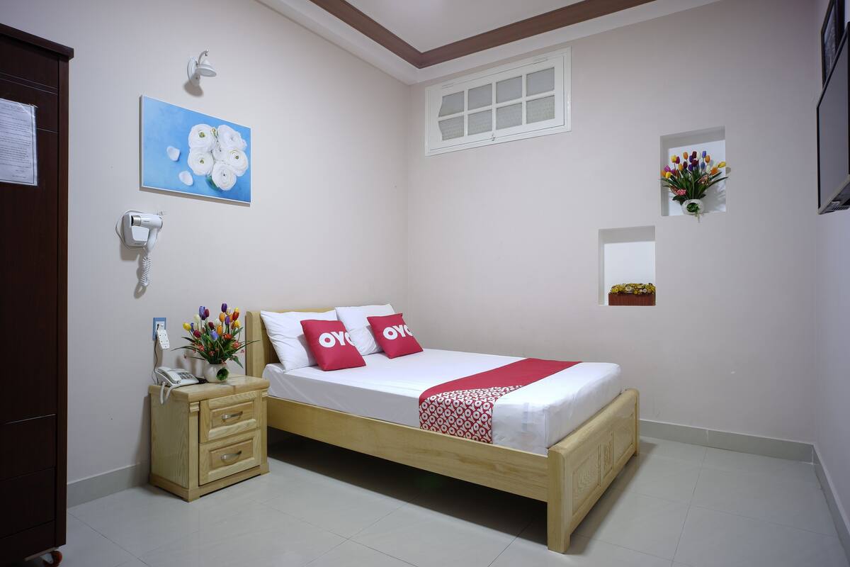Une chambre à coucher avec un lit en bois, du linge de lit blanc, une table de chevet avec un téléphone, une lampe fixée au mur et un tableau.