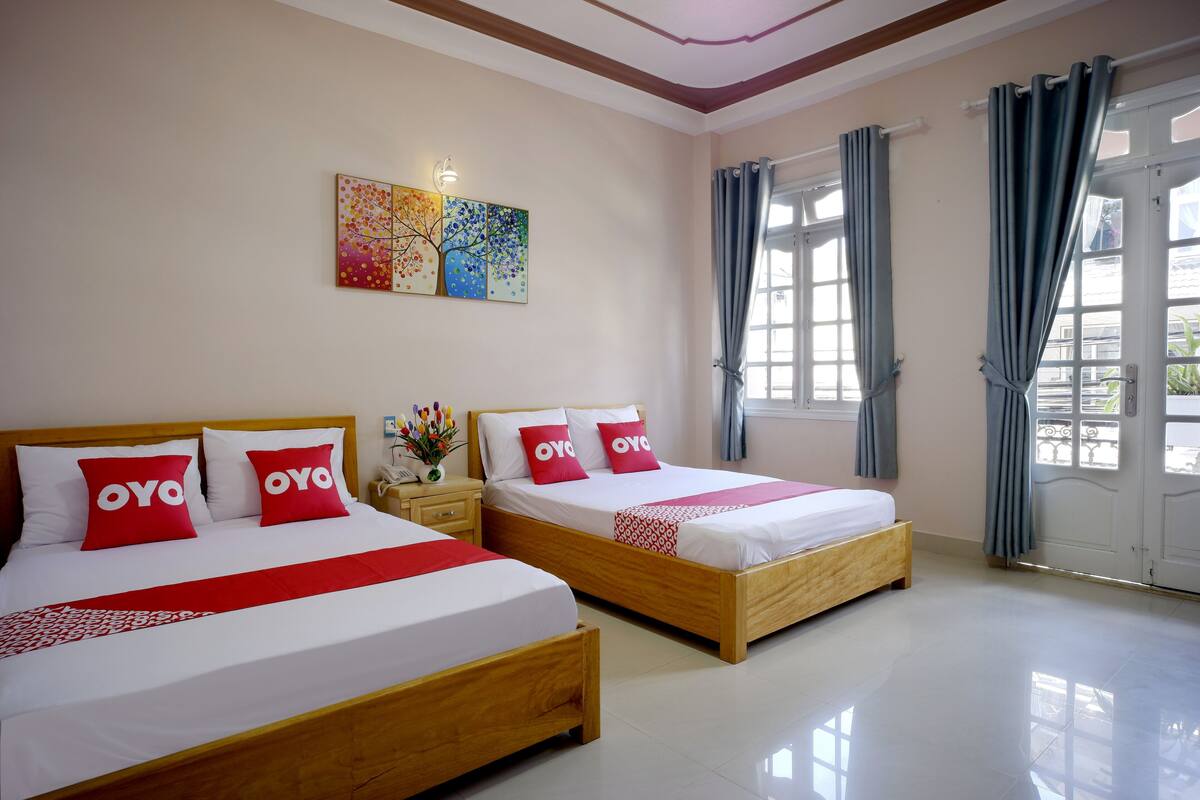 Une chambre d’hôtel avec deux lits, chacun doté d’un cadre en bois et de draps blancs, d’oreillers rouges ornés du logo « OYO » et d’une œuvre d’art colorée accrochée au mur.