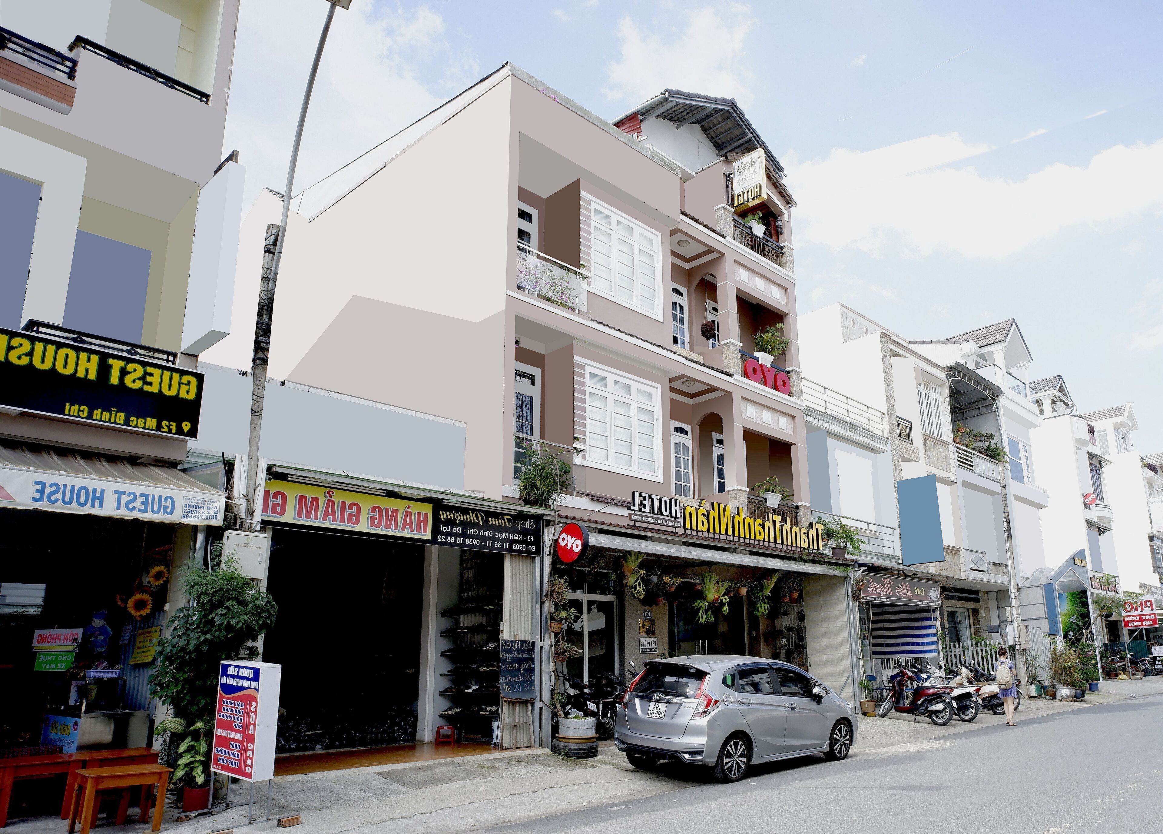 A hotel with a signboard, a car parked in front, and a motorcycle parked on the sidewalk.