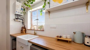 A modern kitchen with a wooden countertop, white cabinets, a built-in dishwasher, a window with a view, and a kettle on the counter.