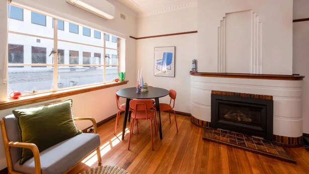 A room with a fireplace, a dining table with chairs, a sofa, and a window with a view of buildings.