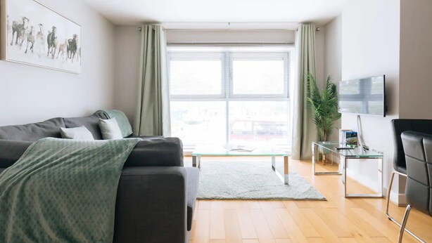 Ein modernes Wohnzimmer mit einer Couch, einem Couchtisch, einem Fernseher und einem Fenster mit Vorhängen.