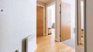 Ein Flur mit Holzboden und weißen Wänden, der zu einem Raum mit einem grauen Sofa und einer Holztür führt.