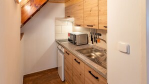 Een kleine keuken met houten kastjes, een roestvrijstalen spoelbak, een magnetron en een broodrooster.