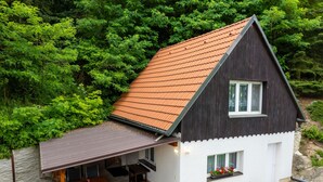 Een woonhuis met twee verdiepingen, een schuin dak, een overdekt terras met een tafel en stoelen, en potplanten op de veranda.