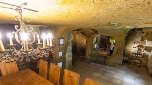 Ein unterirdischer Essbereich mit Holztisch und -stühlen, Steinwänden und einem Kronleuchter.