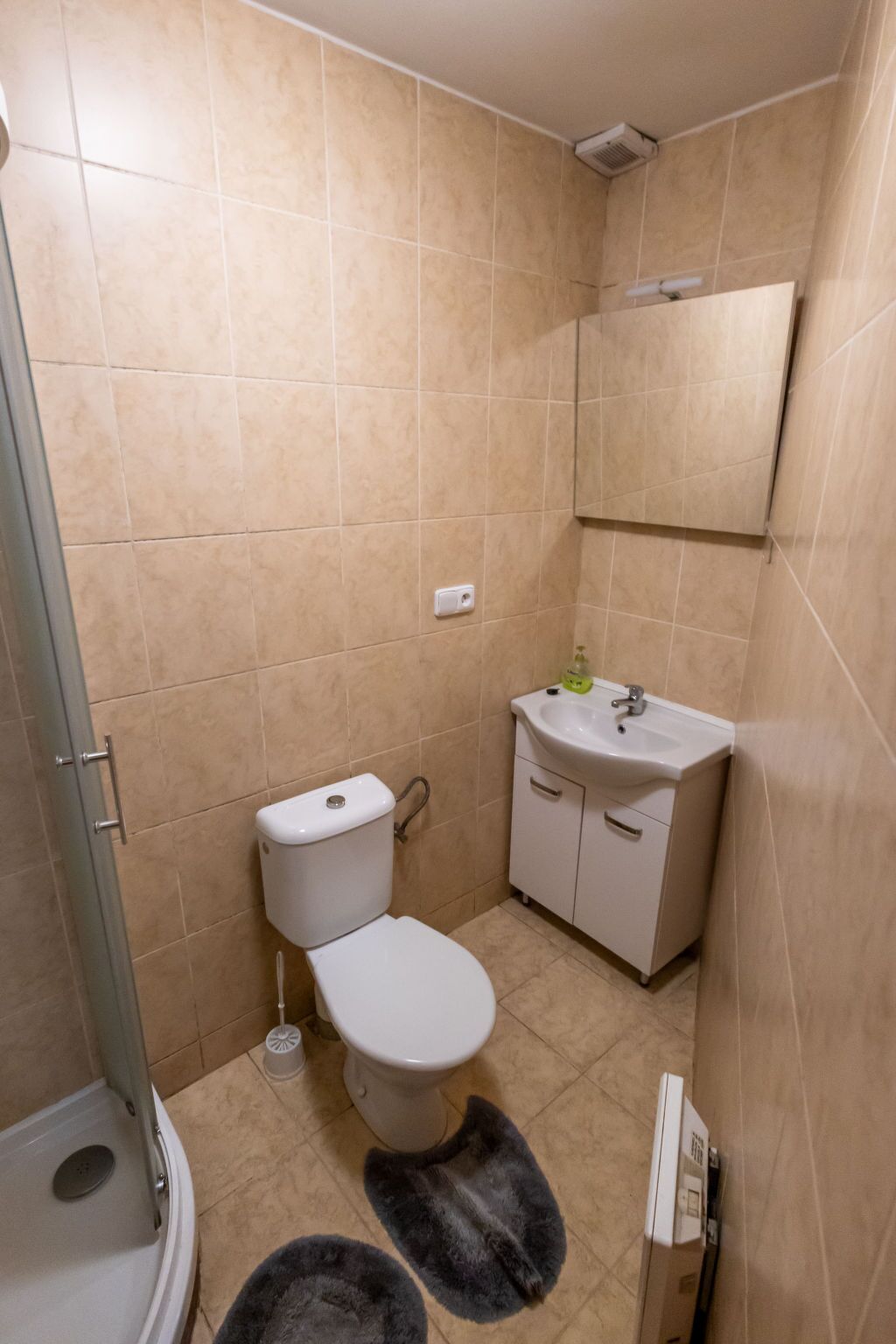 Un bagno con piastrelle color beige, un water, un lavandino e una doccia.