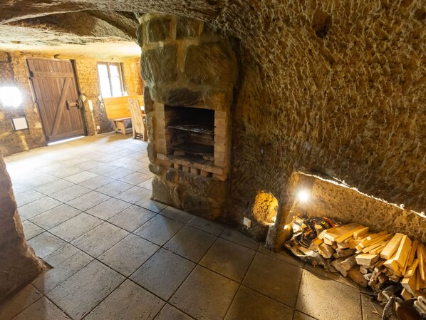 A stone fireplace with a tiled floor, a wooden door, and a stack of firewood.