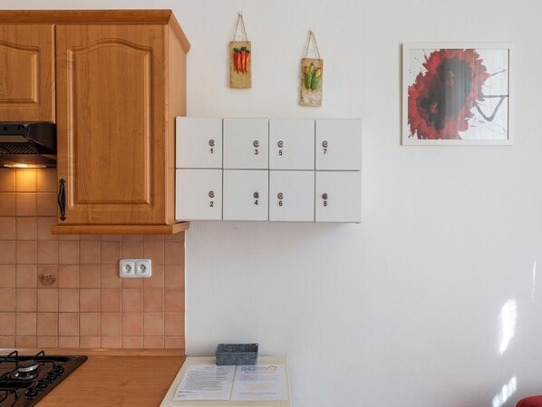 Une cuisine avec des meubles en bois, une cuisinière, un coffre-fort mural à code numérique et un petit îlot central avec un menu.