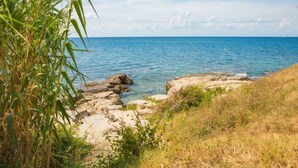 A coastal landscape with clear blue water, rocky outcrops, and green vegetation.