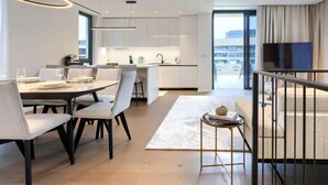 A modern kitchen with white cabinets, a dining area with a table and chairs, and a balcony with a TV.