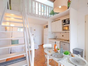 Una cocina moderna con armarios blancos, una mesa de comedor con platos y una escalera que conduce a una zona superior.