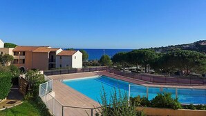 Une piscine avec vue sur la mer, entourée de verdure et de bâtiments.