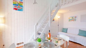 Un salon moderne avec un escalier blanc, une table à manger dressée avec de l’assiette, un canapé et un mur orné d’un tableau.