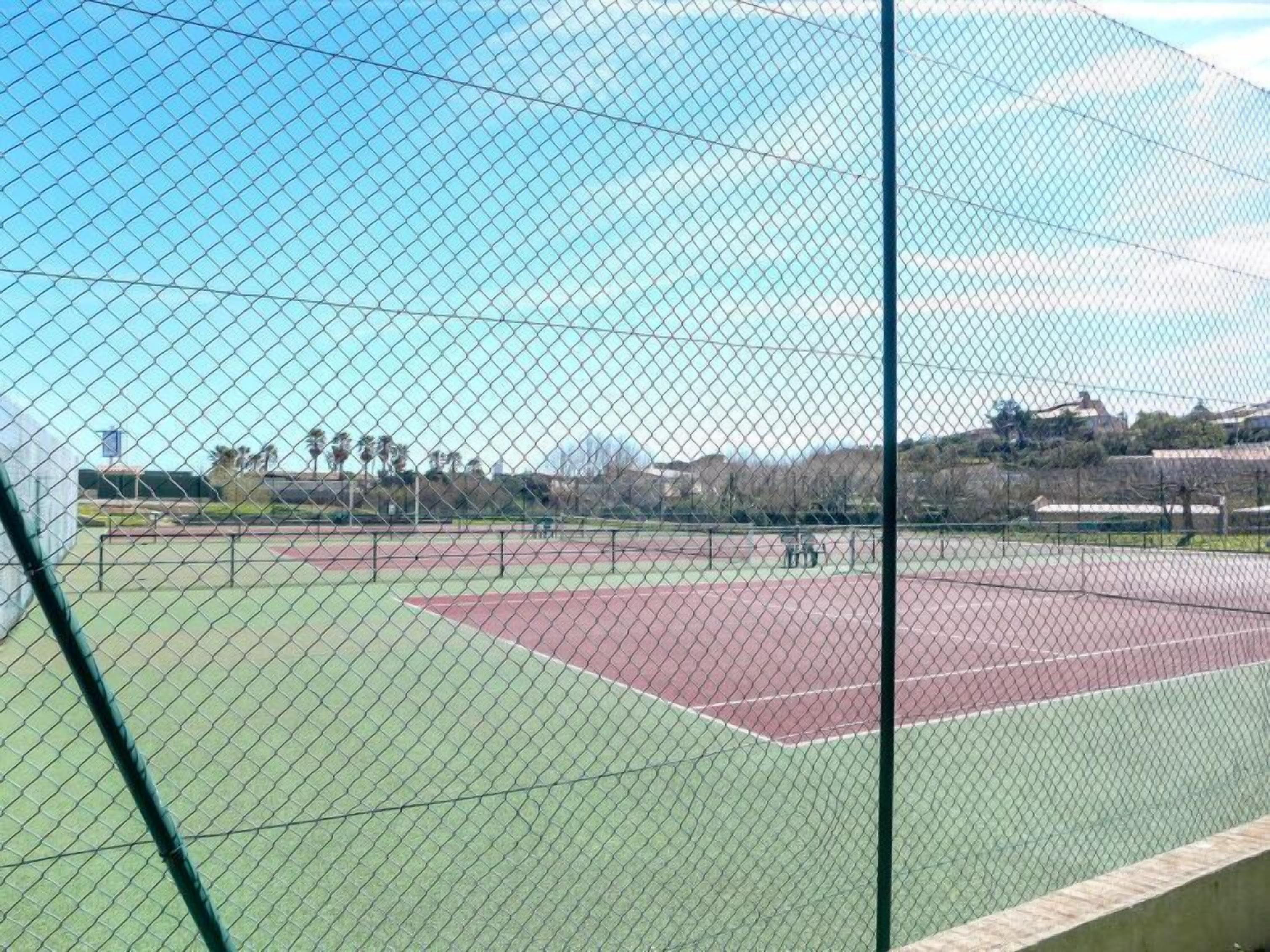 A tennis court enclosed by a chain-link fence with a clear sky in the background.