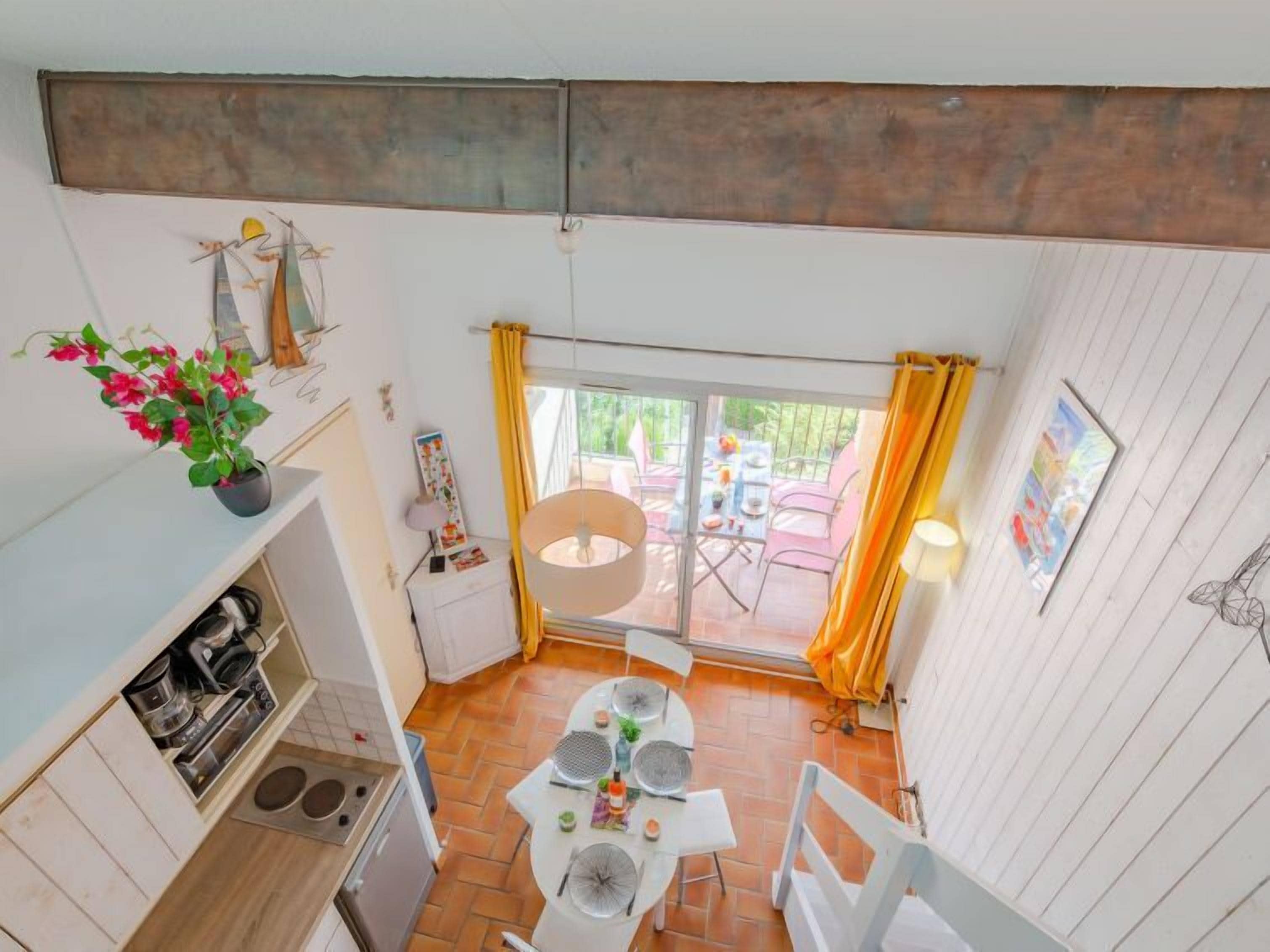 A compact kitchen with a coffee machine, a sink, and a small refrigerator. There is a dining area with a table and chairs, and a sliding glass door leading to an outdoor patio with chairs and a table.