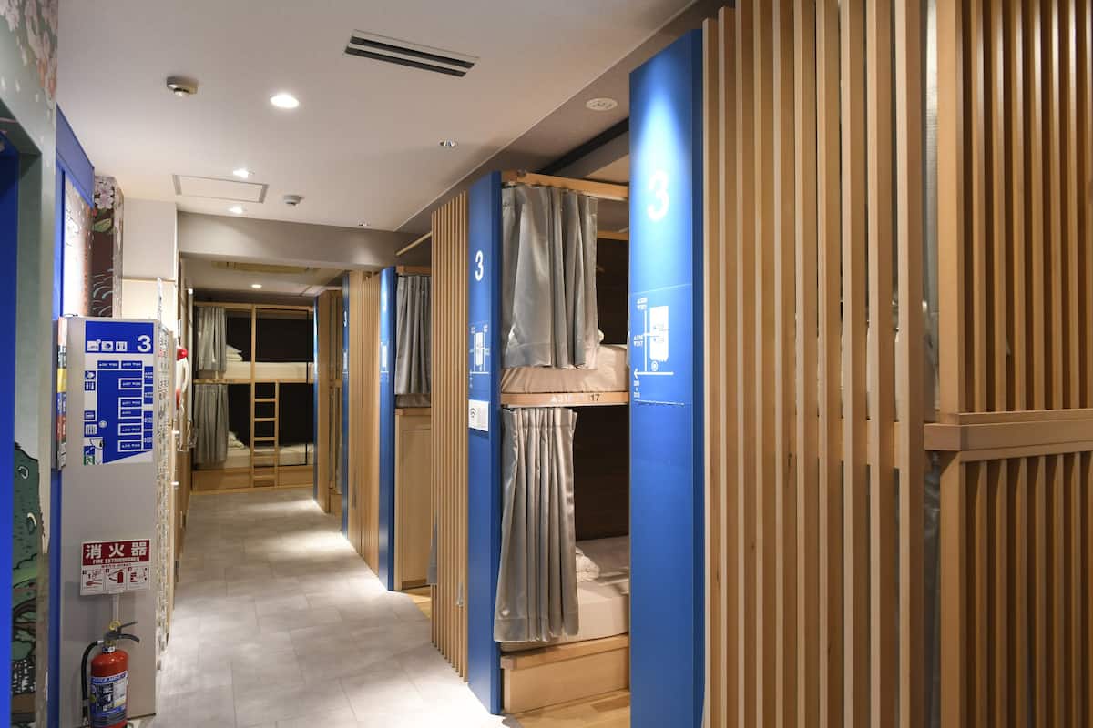 A hotel corridor with bunk beds, blue partitions, and a fire extinguisher.