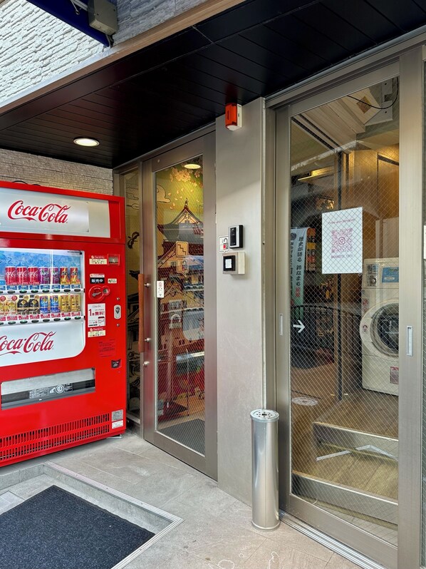 A Coca-Cola vending machine, a glass door entrance, and a washing machine visible through the door.