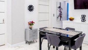 Un comedor moderno con una mesa negra y cuatro sillas, un mueble gris con cajones, un jarrón con flores y un televisor montado en la pared.