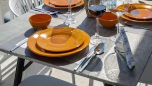 Mesa de comedor dispuesta con platos anaranjados, vasos y cubiertos, con vista a un paisaje urbano.