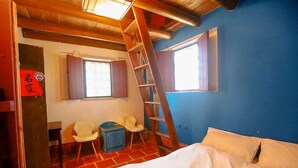 Ein Schlafzimmer mit einem Bett, einer Wendeltreppe, einem Schreibtisch, zwei Stühlen und einem Fenster.