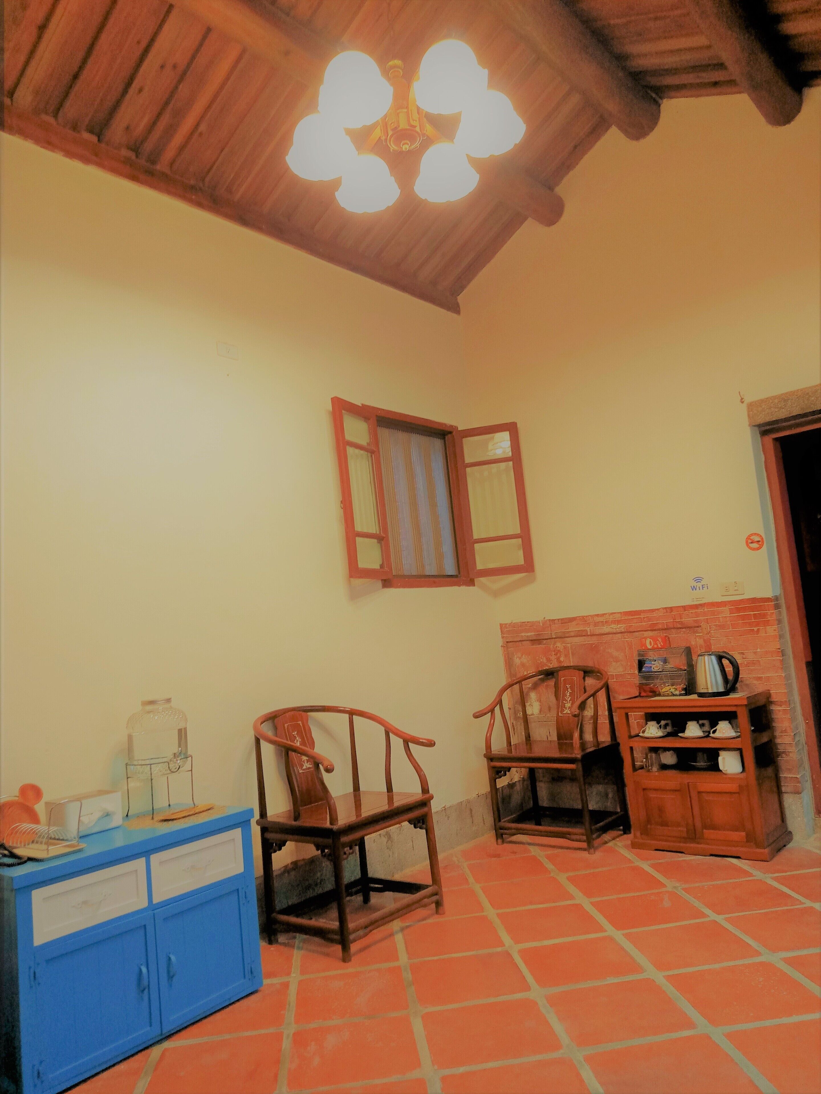 A room with a wooden ceiling, a window with open shutters, a blue cabinet, and a tiled floor.