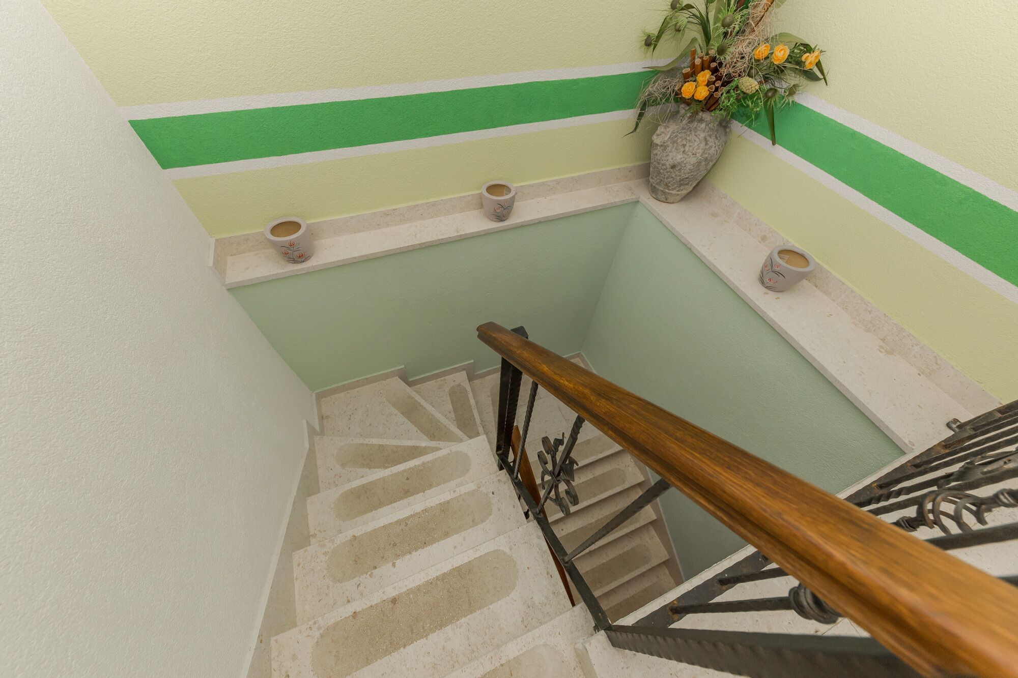Een trap met een houten leuning en een muur met groene en witte strepen.