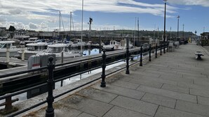 Un puerto deportivo con barcos amarrados, un paseo marítimo y una estatua al fondo.