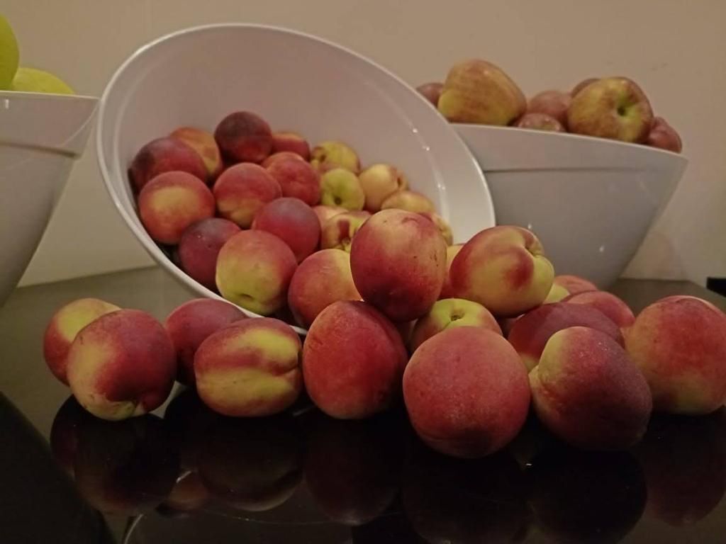 A bowl of red and yellow peaches on a reflective surface.