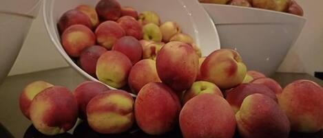 A bowl of red and yellow peaches on a reflective surface.