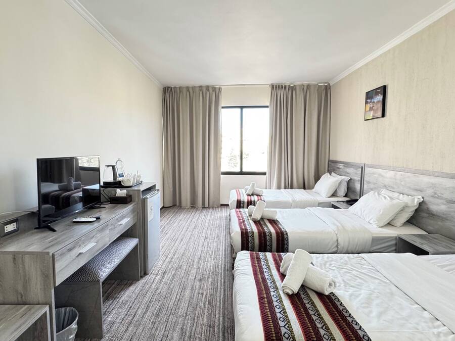 A hotel room with two beds, a desk with a TV, a coffee maker, and a window with curtains.