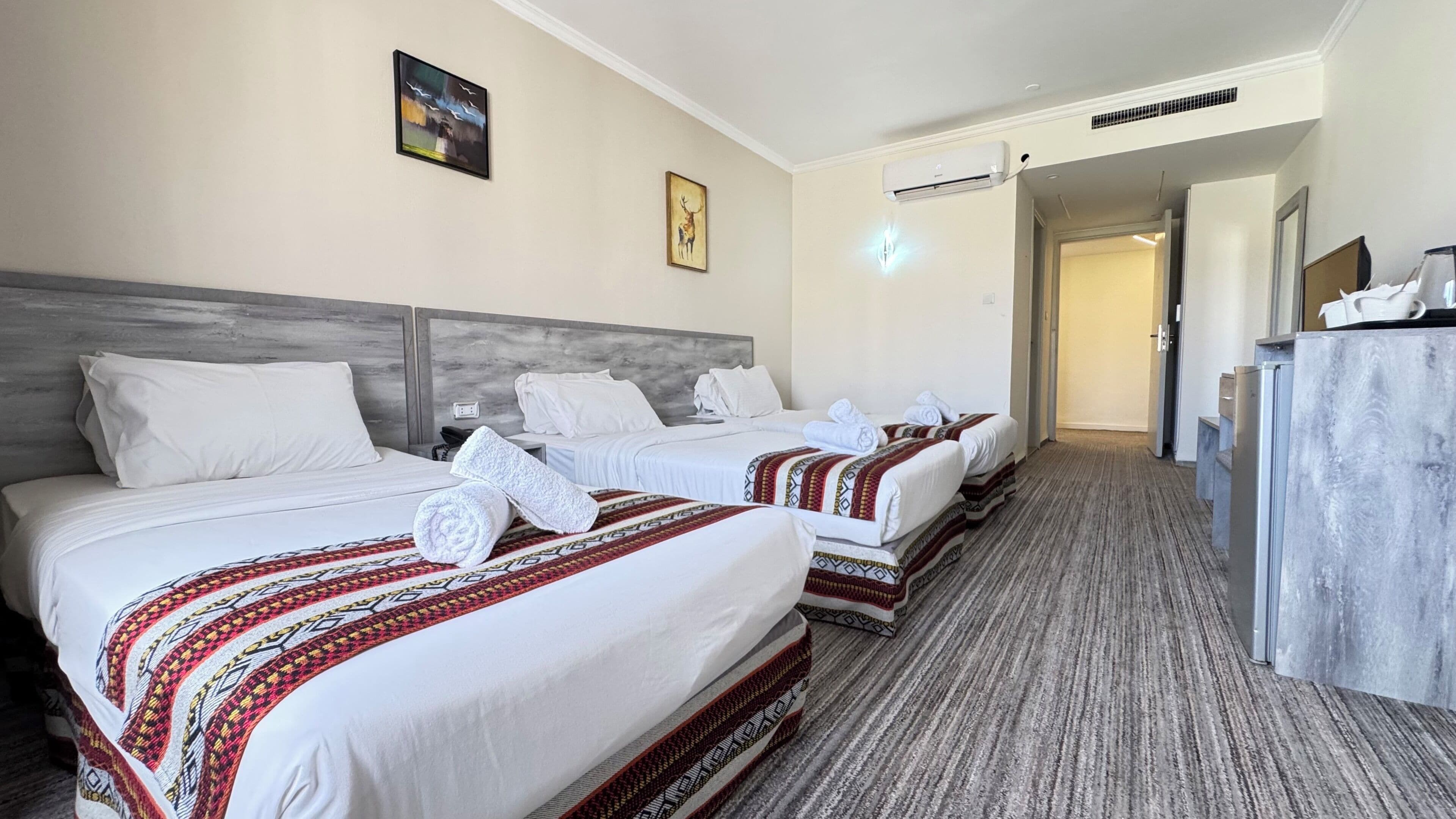 Habitación de hotel con dos camas, un escritorio y una puerta que da a un pasillo.