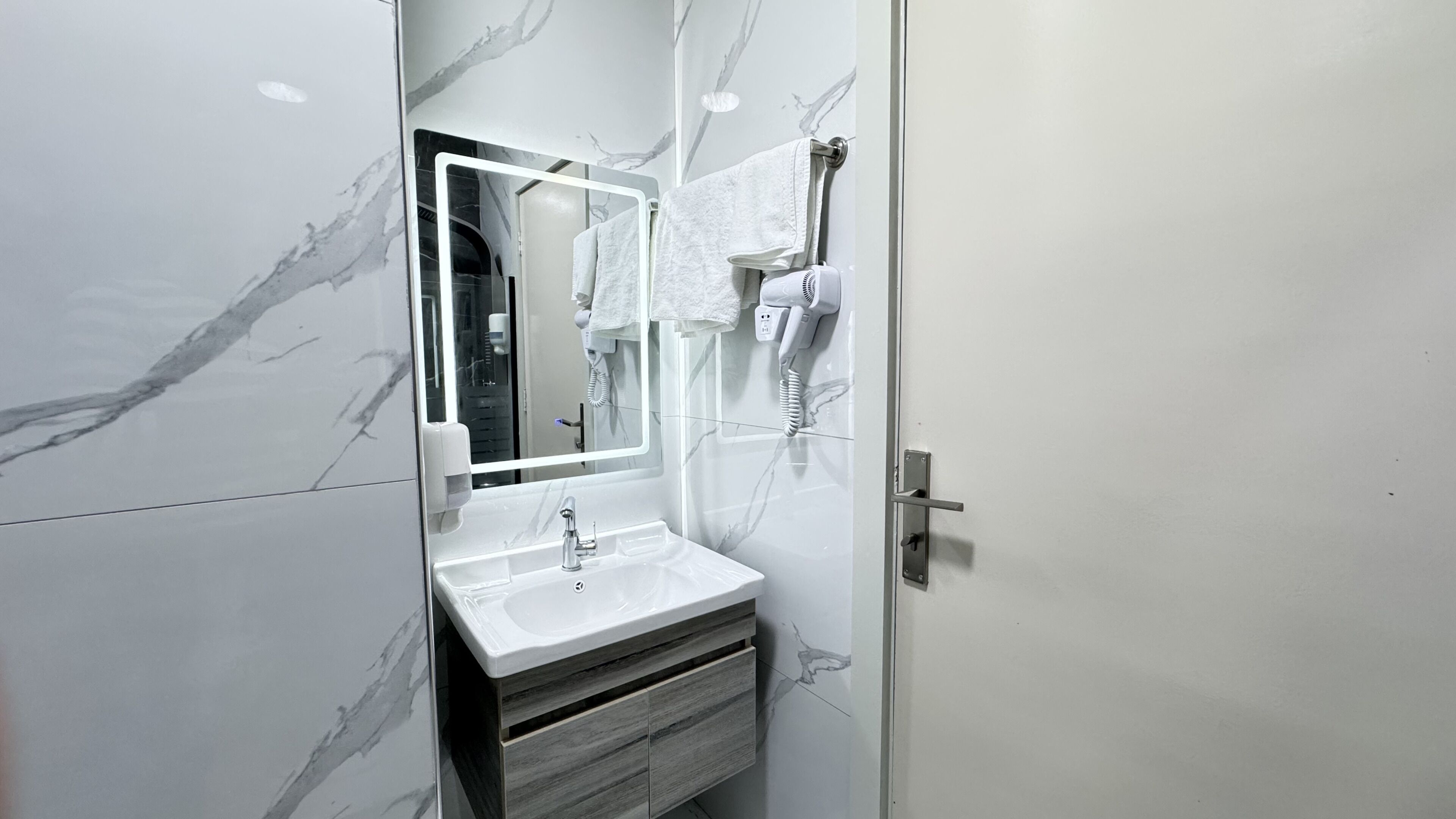A bathroom with a marble wall, a sink with a mirror, and a hairdryer mounted on the wall.