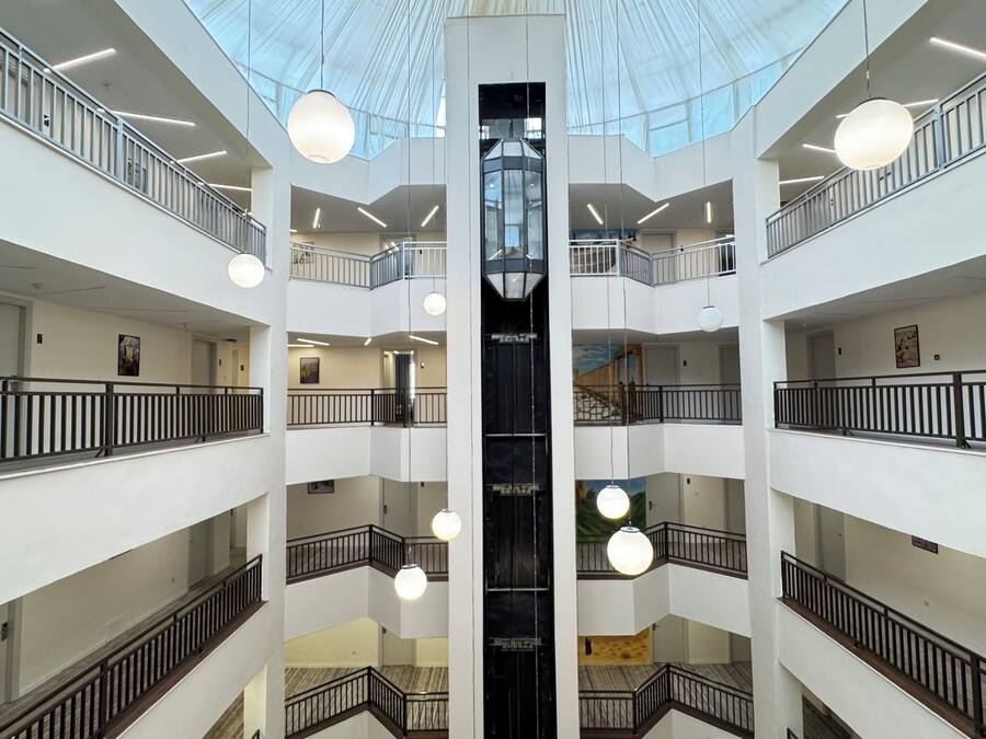 Un atrium à plusieurs niveaux, doté d’un puits d’ascenseur central, de balcons et de luminaires sphériques suspendus.