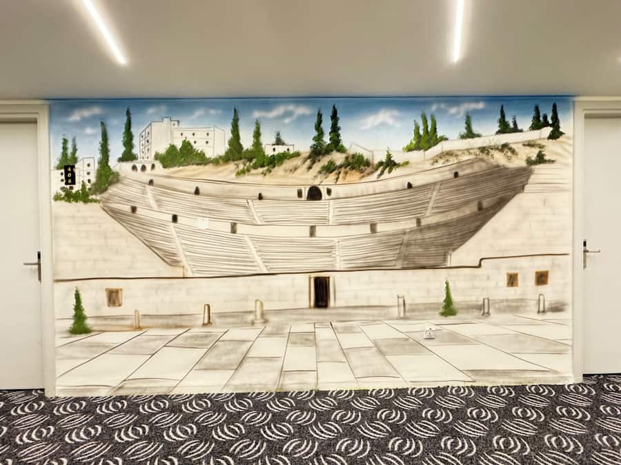 A room with a large mural of an amphitheater, a patterned carpet, and white doors.