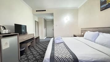 A hotel room with a bed, a desk with a television, a coffee machine, and a door leading to another room.