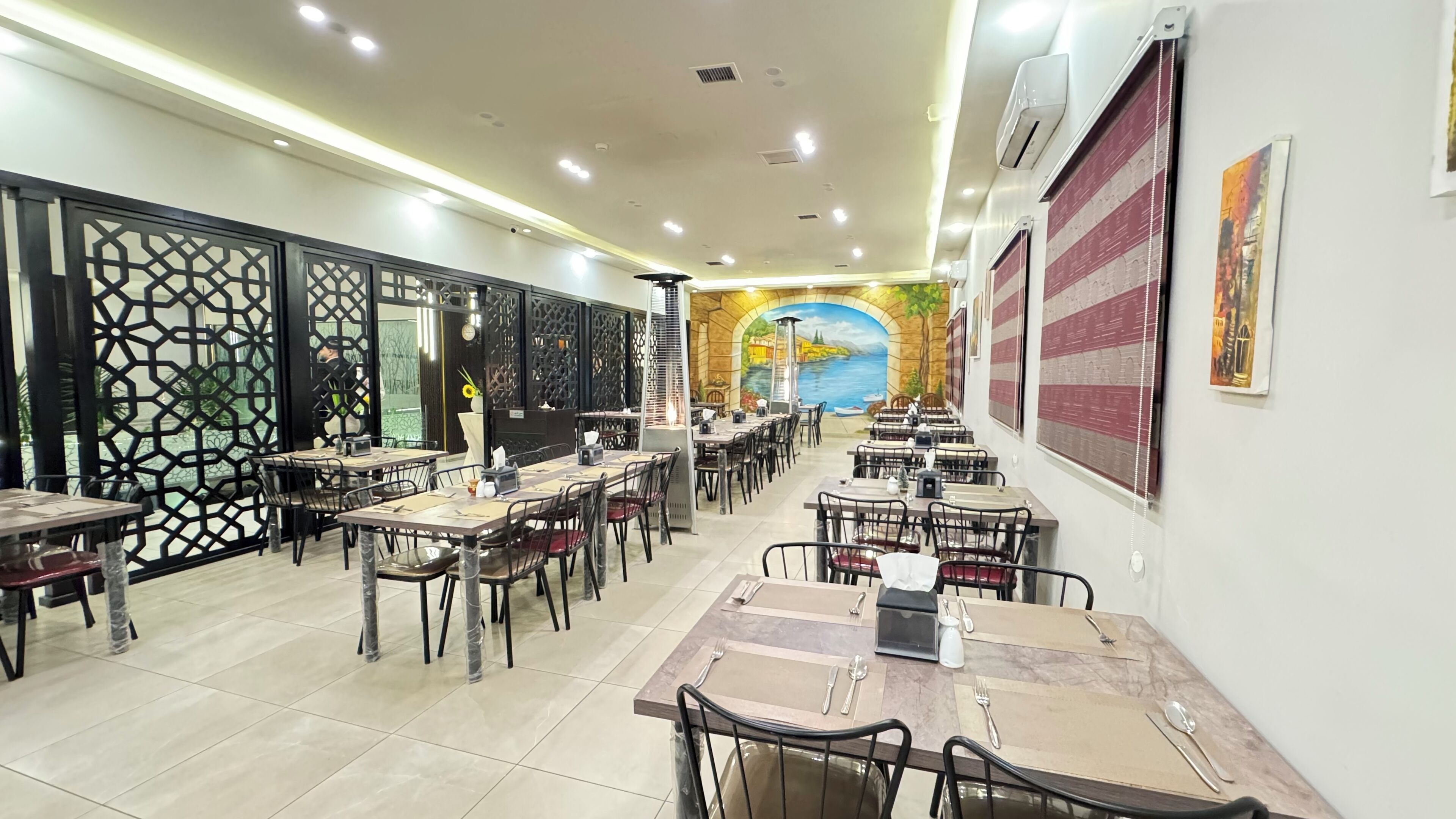 A restaurant with multiple tables and chairs, a decorative wall mural, and a patterned ceiling.