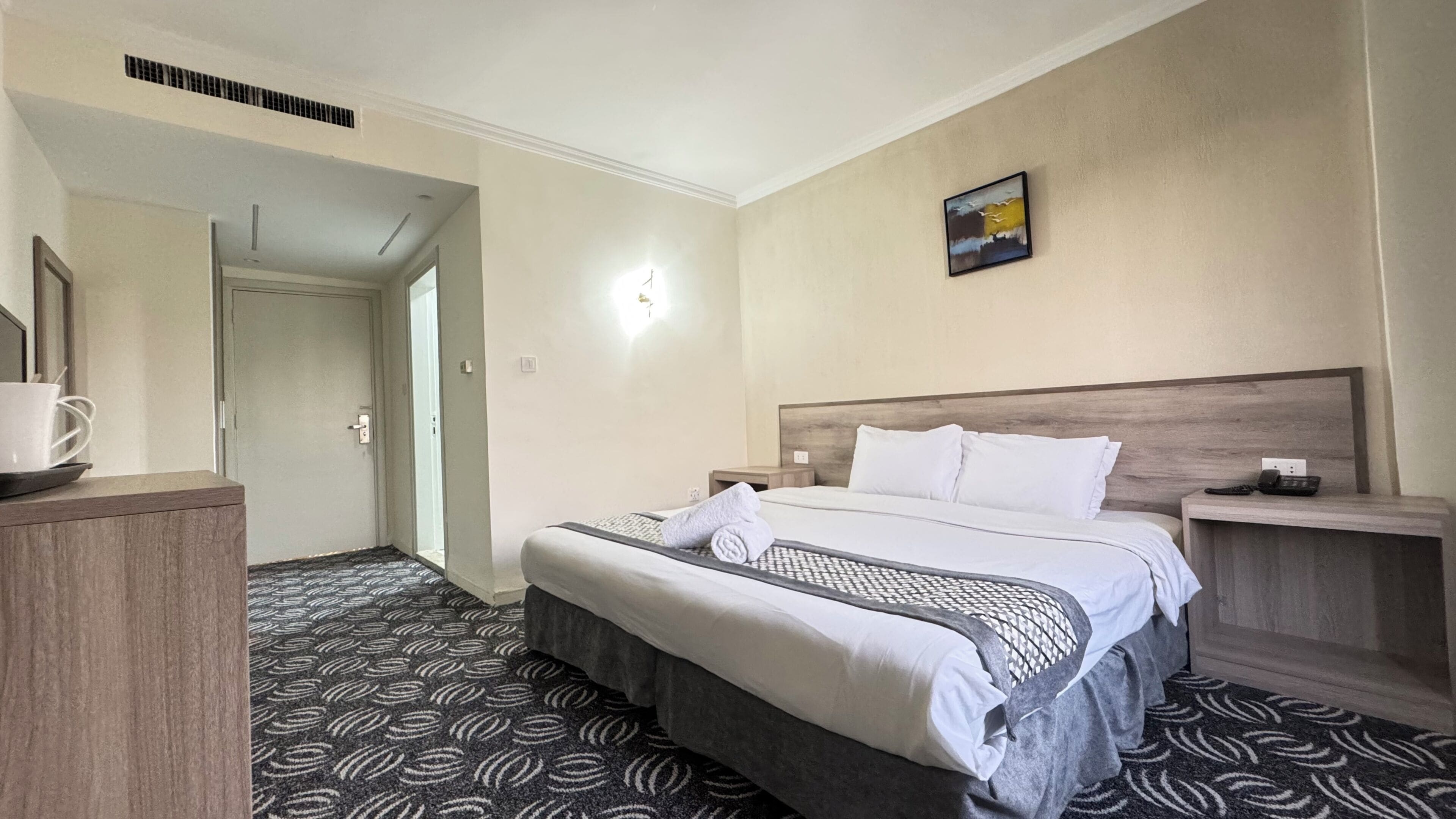 A hotel room with a bed, bedside tables, a telephone, and a painting on the wall.