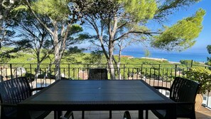 A table with chairs on a balcony overlooking a scenic view of the sea and greenery.