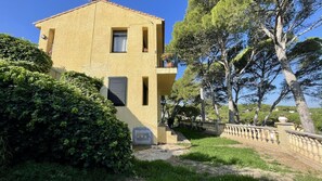 A two-story building with a yellow facade, a small balcony, and a garden area with trees and shrubs. - CASA GLORIA BEGUR (Begur)